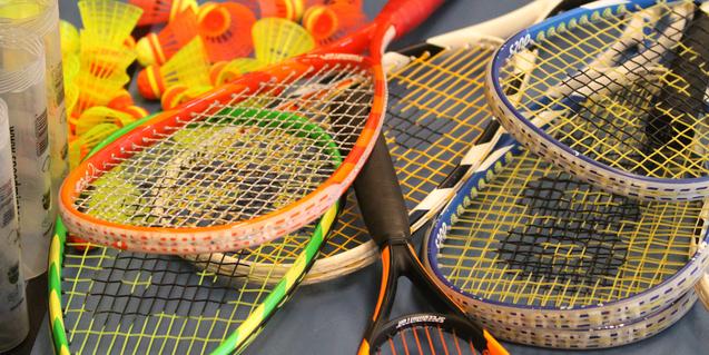 Bunte Badminton-Schläger und -Bälle liegen auf einem Tisch, umgeben von transparenten Schutzhüllen.