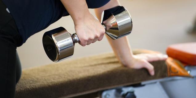 Frau macht eine Bizepsübung mit einer Hantel, während sie auf einer Trainingsbank lehnt.