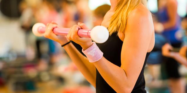 Frau hält eine pinke Hantel mit weißen Enden, während sie in einem Fitnessstudio trainiert.