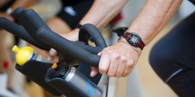 Nahaufnahme von Händen, die an den Lenkern eines Spin- und Getränkeflaschenhalter eines Fitnessbikes greifen.