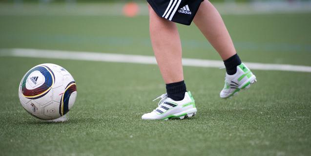 Ein Fuß mit Fußballschuhen tritt auf einen Fußball auf einem Kunstrasenfeld.