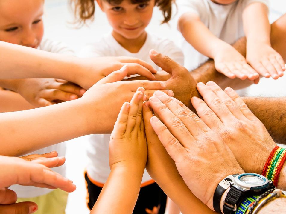 Kinder und Erwachsene legen ihre Hände in einem Kreis zusammen, symbolisieren Zusammenarbeit und Gemeinschaft.