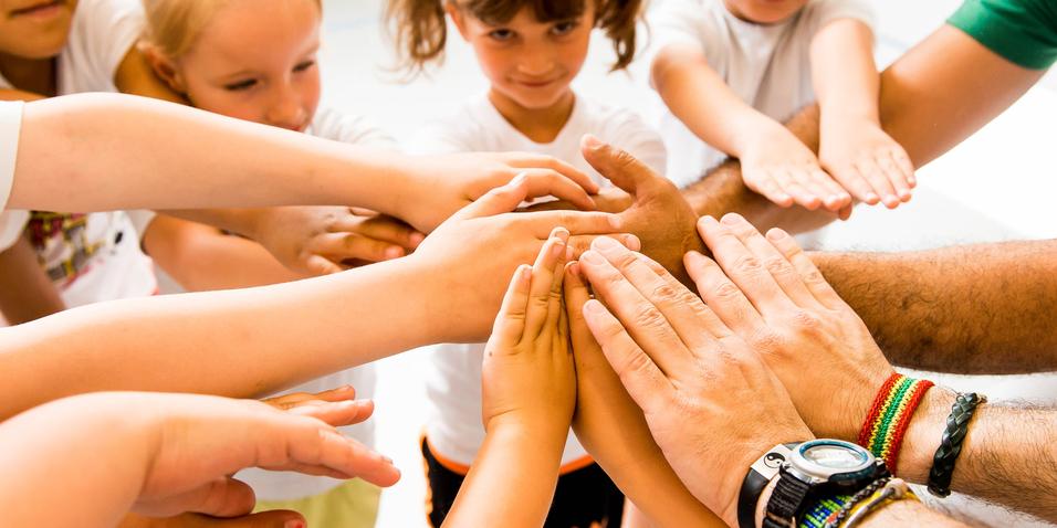 Kinder und Erwachsene legen ihre Hände in einem Kreis zusammen, symbolisieren Zusammenarbeit und Gemeinschaft.