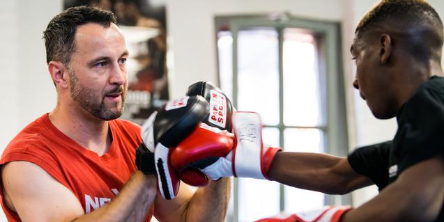 Trainer überwacht das Boxtraining eines Schülers, beide tragen Boxhandschuhe in einem Trainingsraum.