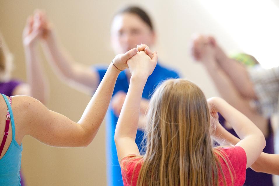Gruppe von Kindern hält sich in einem gemeinsamen Kreis an den Händen, während sie in einer Sporthalle aktiv sind.