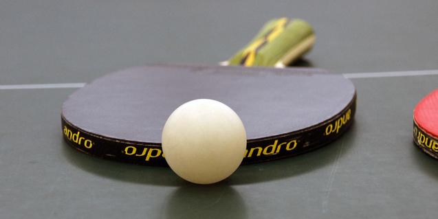 Nahaufnahme eines Tischtennisschlägers mit weißem Ball auf einer grünen Tischtennisplatte.