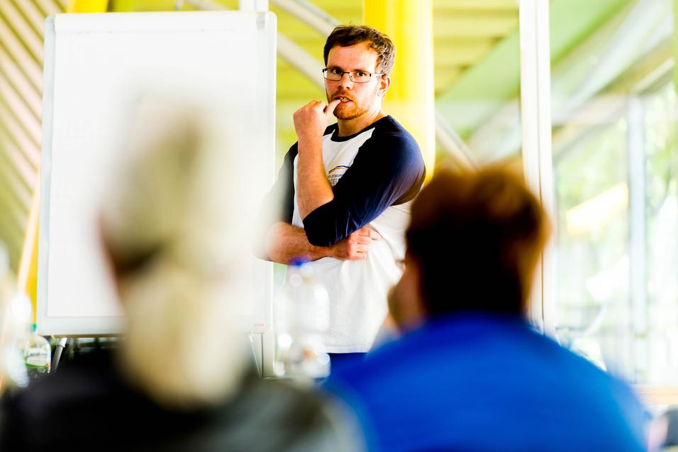 Mann mit Brille spricht vor einer Gruppe, ein Flipchart ist im Hintergrund sichtbar.