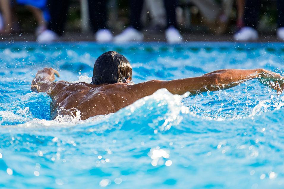 Schwimmer mit freiem Oberkörper, der im Wasser auf dem Rücken schwimmt, umgeben von spritzendem Wasser.